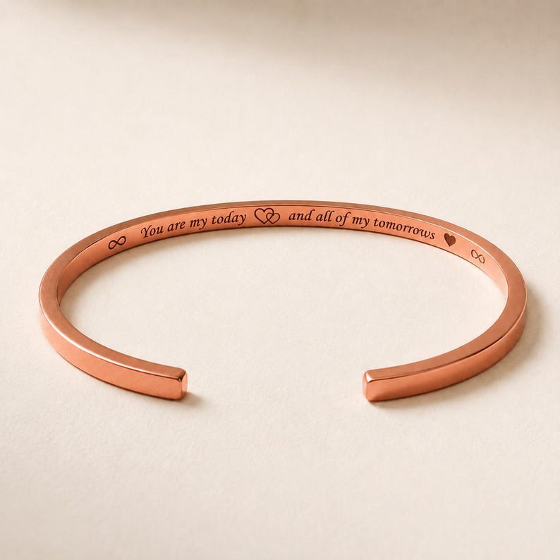 May include: A rose gold-toned cuff bracelet featuring an open design. The outer surface is engraved with the text "You are my today and all of my tomorrows" accompanied by an infinity symbol, two interlocking hearts, and a small heart icon.