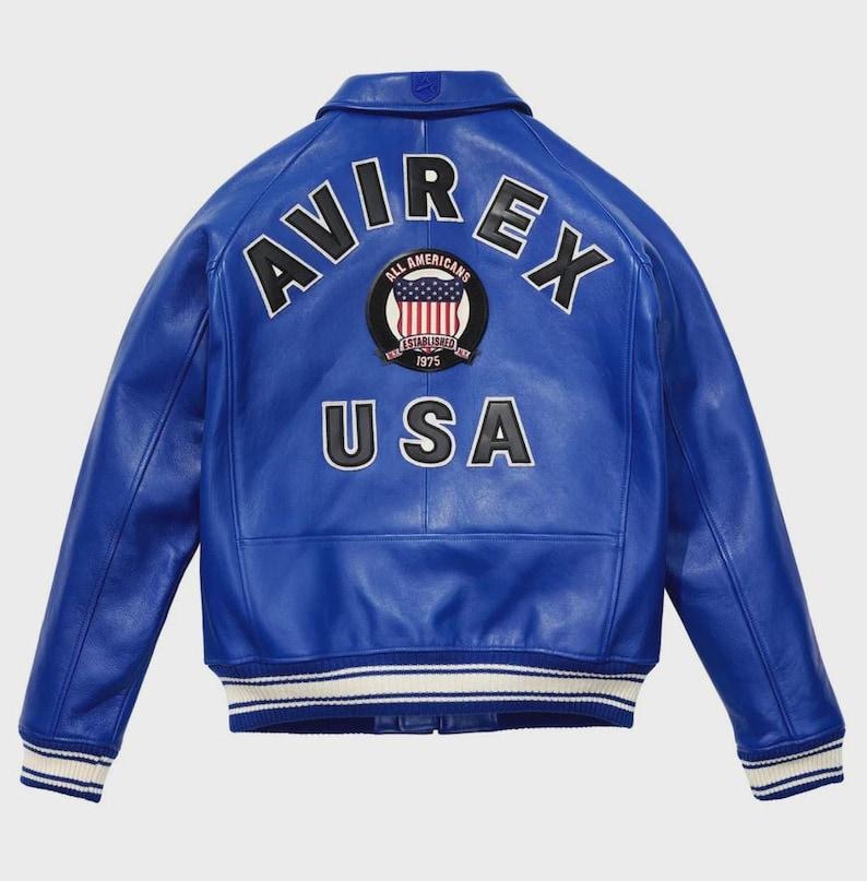 May include: A vibrant blue leather jacket with the word "AVIREX" arched across the shoulders in white block letters. Below, "USA" is displayed. A circular patch with the American flag and the words "ALL AMERICANS ESTABLISHED 1975" is centered.