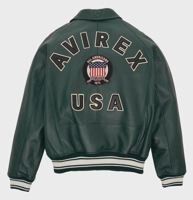 May include: A dark green leather jacket with the word "AVIREX" arched across the shoulders. Below is a patch with the American flag and the words "ALL AMERICANS ESTABLISHED 1975". The word "USA" is below the patch. The jacket has white and green striped cuffs and hem.