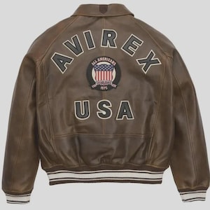 May include: Brown leather jacket with the word "AVIREX" across the back in white lettering. Below the word "AVIREX" is a circular patch with the words "ALL AMERICANS" and "ESTABLISHED 1975" surrounding a design of the American flag. The word "USA" is below the patch.