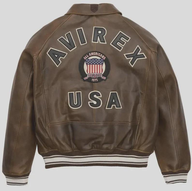 May include: Brown leather jacket with the word "AVIREX" across the back in white lettering. Below the word "AVIREX" is a circular patch with the words "ALL AMERICANS" and "ESTABLISHED 1975" surrounding a design of the American flag. The word "USA" is below the patch.