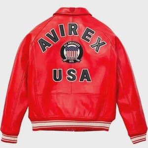 May include: A vibrant red leather jacket with the text "AVIREX" arched across the shoulders and "USA" below a circular emblem. The emblem features a shield with the American flag and the words "ALL AMERICANS ESTABLISHED 1975". The jacket has white and black striped cuffs.