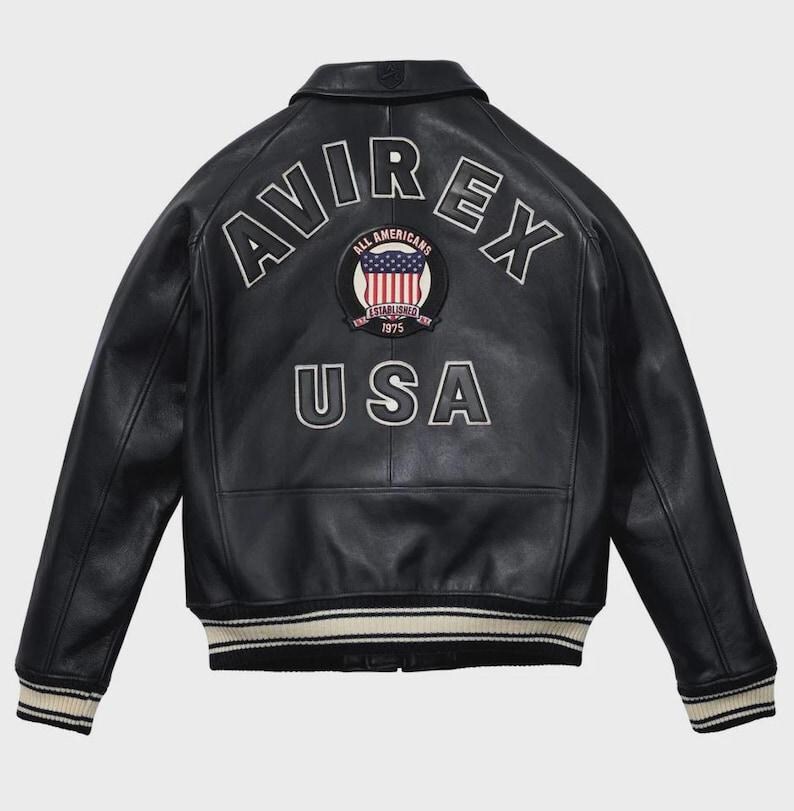 May include: Black leather jacket with the word "AVIREX" arched across the back in white lettering. Below the word "AVIREX" is a circular patch with the words "ALL AMERICANS ESTABLISHED 1975" and a US flag design. The word "USA" is below the patch.