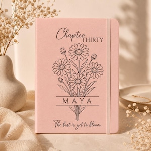 Könnte beinhalten: Ein hellrosa Notizbuch mit einer schwarzen Strichzeichnung eines Gänseblümchenstraußes. Der Text lautet Chapter THIRTY, MAYA und The best is yet to bloom. Der Einband hat einen vertikalen elastischen Verschluss an der rechten Vorderseite.