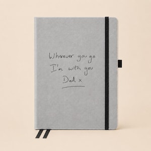 May include: A light gray notebook with a black elastic closure and a black pen loop. The front cover features the black printed text: Wherever you go I'm with you Dad x. The notebook includes two black ribbon bookmarks extending from the bottom edge.