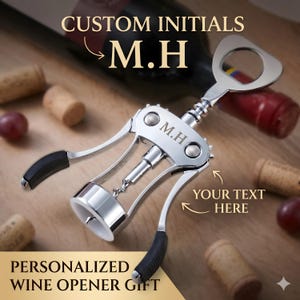 May include: A silver-coloured metal wine opener with two side levers featuring black rubber grips and a central corkscrew mechanism. The metal body is engraved with the initials M.H. The top of the device includes a built-in bottle cap opener.