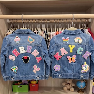 May include: Two blue denim jackets with patches and names. One jacket says "SERENA" with a Minnie Mouse patch, a cupcake, a butterfly, and a diamond. The other jacket says "KAYCE" with a butterfly, a rainbow, a flower, and a unicorn.