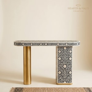 Könnte beinhalten: Dekorative Konsole mit floralem Schwarz-Weiß-Muster auf der Tischplatte und einem Bein. Das andere Bein ist ein goldener Zylinder. Der Text "HEARTH & HALO CREATION" ist vorhanden.