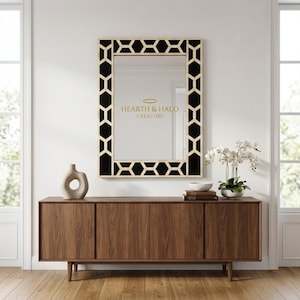 May include: A rectangular wall mirror with a black and light wood geometric frame featuring a repeating hexagonal pattern. The mirror surface displays the gold text HEARTH & HALO CREATION. It is positioned above a long wooden sideboard cabinet.