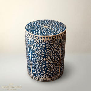 May include: A cylindrical side table with a navy blue background and a cream-colored leaf pattern. The top is divided into four sections. The table is approximately 18 inches tall and 16 inches in diameter.