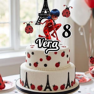 May include: A two-tier white cake decorated with red and black ladybug spots and black Eiffel Tower silhouettes. A cake topper features a Miraculous Ladybug character, a black Eiffel Tower, the name Vera, and the number 8 in black and white.
