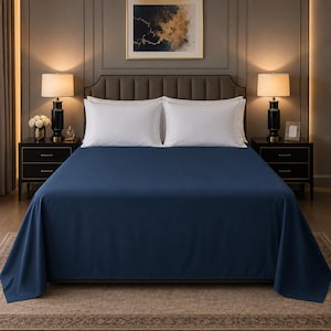 Peut inclure: Un drap plat de couleur bleu marine foncé uni recouvrant un lit avec deux oreillers rectangulaires blancs. Le drap présente une texture lisse et mate, couvrant toute la surface du matelas et retombant sur les côtés du cadre de lit.