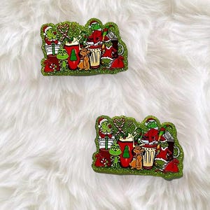 May include: Two glittery, green-bordered acrylic pins featuring a festive illustration of the Grinch, a dog, and various holiday-themed mugs, candy canes, and gift bags. The colourful design includes red, white, and green accents throughout.