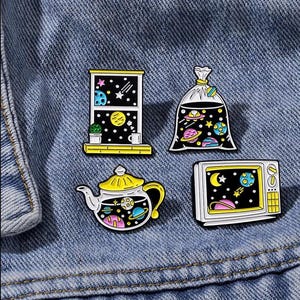 Pode incluir: Quatro pins de esmalte com temas espaciais: uma janela com vista para estrelas e planetas, um saco plástico cheio de corpos celestes, um bule contendo uma galáxia e uma televisão vintage exibindo uma lua, estrelas e planetas.