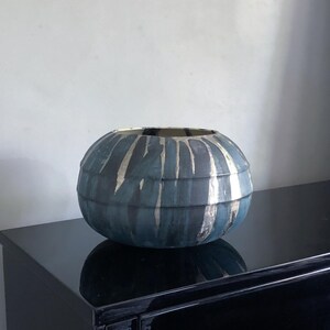 May include: A spherical, blue decorative vase with vertical silver stripes. The vase has a textured finish and a wide opening. The vase is on a black surface.