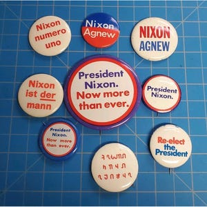May include: A selection of vintage political campaign badges. The badges feature text such as "Nixon Agnew", "President Nixon", and "Re-elect the President". The badges are in various colours, including red, white, and blue.