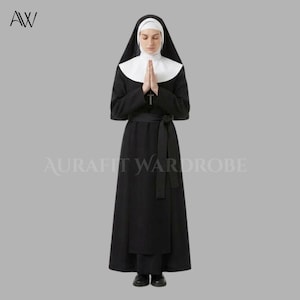 Puede incluir: Un hábito de monja negro que consiste en un vestido largo de manga larga con un cinturón de lazo a juego, una toca blanca y un velo negro. Un colgante de cruz plateada cuelga del cuello. El texto AURAFIT WARDROBE es visible en el centro.