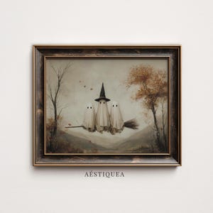May include: A framed wall art print featuring three white ghosts riding a broomstick against an autumn landscape with trees and mountains. The central ghost wears a black pointed hat. The text AÉSTIQUEA is printed in black below the frame.