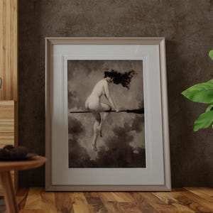 May include: A framed sepia-toned art print featuring a figure with long dark hair flying through a cloudy sky while seated on a broomstick. The artwork is enclosed in a light-colored rectangular frame with a white mat border, displayed vertically.