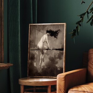 May include: A framed sepia-toned art print depicting a figure with long flowing hair riding a broomstick through a cloudy sky. The artwork features a monochromatic palette with dark shadows and light highlights, presented in a thin gold frame.