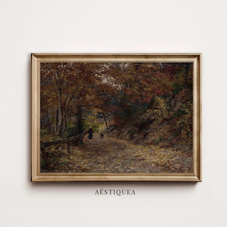 Puede incluir: Un cuadro de paisaje enmarcado que representa un camino de tierra que serpentea a trav&eacute;s de un bosque denso durante el oto&ntilde;o. La escena muestra &aacute;rboles con follaje marr&oacute;n y naranja, una persona paseando a un perro y una valla de madera, todo en un marco dorado.