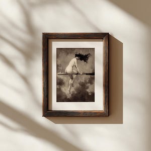 May include: A framed art print featuring a sepia-toned illustration of a figure with long flowing hair riding a broomstick through a cloudy sky. The artwork is enclosed in a dark, textured wooden frame with a light-colored mat border.