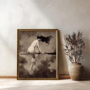May include: A framed sepia-toned art print depicting a figure with long flowing hair riding a broomstick through a cloudy sky. The artwork is enclosed in a thin gold-colored frame, showcasing a monochromatic scene with dramatic shadows and highlights.