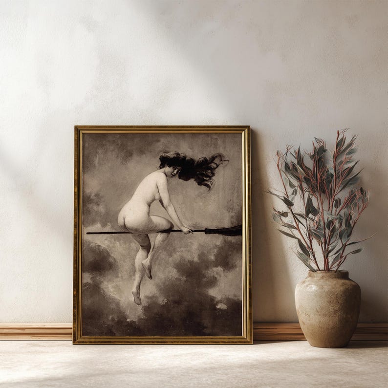 May include: A framed sepia-toned art print depicting a figure with long flowing hair riding a broomstick through a cloudy sky. The artwork is enclosed in a thin gold-colored frame, showcasing a monochromatic scene with dramatic shadows and highlights.
