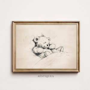 Pode incluir: Uma impressão de arte de parede horizontal emoldurada apresentando um esboço em tinta preta de um urso de pelúcia dormindo sob um cobertor. O desenho é feito em um estilo solto e expressivo sobre um fundo bege claro. O texto AESTIQUEA está impresso abaixo.