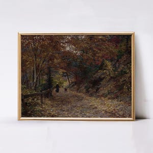 Puede incluir: Un cuadro de paisaje enmarcado que representa un sendero forestal en oto&ntilde;o. La escena muestra &aacute;rboles altos con follaje marr&oacute;n y naranja, una ladera rocosa y una persona paseando a un perro por un camino cubierto de hojas con una valla.