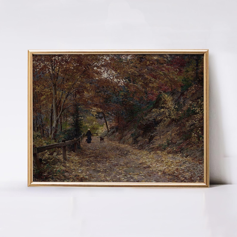 Puede incluir: Un cuadro de paisaje enmarcado que representa un sendero forestal en oto&ntilde;o. La escena muestra &aacute;rboles altos con follaje marr&oacute;n y naranja, una ladera rocosa y una persona paseando a un perro por un camino cubierto de hojas con una valla.