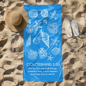 May include: A blue beach towel featuring white seashell and starfish designs. The towel has the text "COLOSSIANS 1:16" and a Bible verse. A straw sun hat and white flip-flops are also visible on the sand.