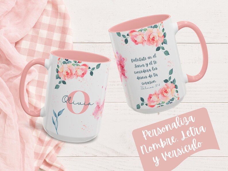 May include: Two white ceramic mugs with pink interiors and handles. Floral designs with pink roses and green leaves decorate the mugs. One mug has the name "Olivia" and a letter "O". The other mug has Spanish text. The mugs are on a pink and white checkered background.