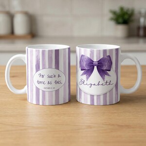 Puede incluir: Dos tazas de cerámica blanca con rayas moradas de acuarela. Una taza tiene el texto "For such a time as this." y la otra tiene un lazo morado y el nombre "Elizabeth". Ambas tazas tienen asas blancas.