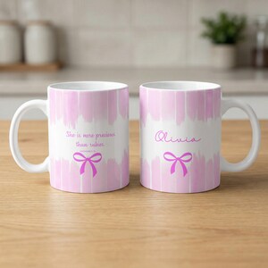 Peut inclure: Deux mugs en céramique blanche avec des motifs roses en coups de pinceau. L'un des mugs porte l'inscription "She is more precious than rubies" et un nœud rose. L'autre mug porte le nom "Olivia" et un nœud rose.