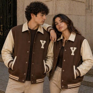 May include: Brown and cream varsity jackets featuring the letter "Y". The jackets have cream sleeves and collars, brown bodies and pockets. The jackets are worn with neutral-coloured trousers.