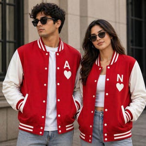 May include: Red and white letterman jackets with white sleeves. Each jacket has a white heart and a letter, one with an "A" and the other with an "N". The jackets have white stripes on the cuffs and bottom.