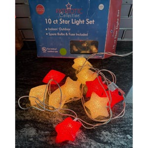 May include: A string of star-shaped lights in red and yellow, with a white wire. The box reads "Patriotic Collection 10 ct Star Light Set" and includes spare bulbs and a fuse. For indoor/outdoor use.