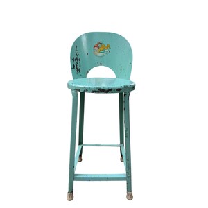 May include: A light blue metal stool with a distressed finish and four legs. The backrest features a small, colorful graphic of a cartoon character resting in a teacup. The stool has a circular seat and a curved backrest with a cutout section.