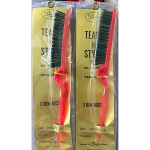 May include: Two packaged hair teasing brushes. Each brush has a red handle and a black bristle head. The packaging is gold with black text that reads "TEASING STYLE" and "3 ROW BRISTLE". The brand name "Diane" is also visible.