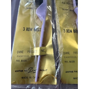 Könnte beinhalten: Mehrere Packungen Haarteaser-Bürsten sind sichtbar. Die Bürsten sind lila und schwarz, und die Verpackung ist goldfarben mit schwarzem Text. Der Text auf der Verpackung lautet "3 Row Brist" und "Diane Products Inc."