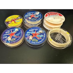 May include: A selection of clear plastic spools of elastic cord for jewellery making. The spools are labelled with the brand name "Stretch Magic" and various measurements in mm and meters. The labels are yellow, blue, and white.