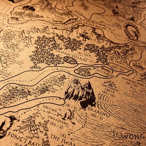 May include: A detailed map in a vintage style, with black line art on a tan background. It features locations such as "Gaipan Village" and "Omashu." The map depicts mountains, forests, and waterways, creating a sense of adventure.