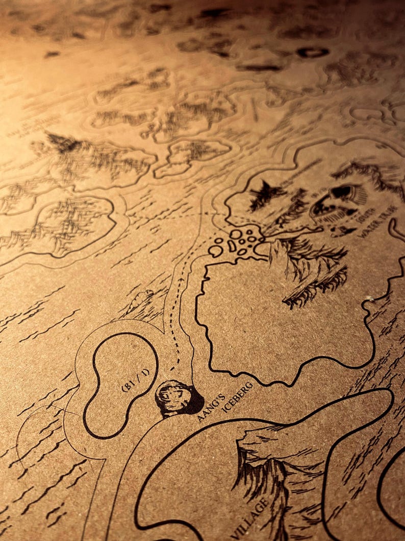 May include: A detailed map with black line art on a tan background. The map features geographical details, including landmasses, coastlines, and the text "Aang's Iceberg" and "Village". The map has a vintage, hand-drawn aesthetic.