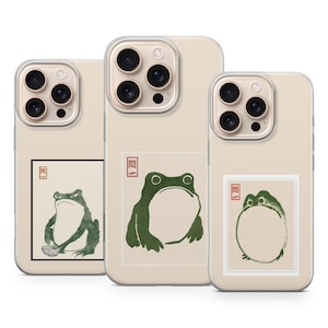 May include: Three phone cases with a beige background. Each case features a different green frog illustration in a Japanese woodblock style. The cases have a clear border around the camera.