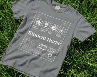 May include: A grey t-shirt featuring the words "Student Nurse" in white. The shirt has a graphic with icons and text, including "Keep indoors," "Requires coffee," and "Multi-tasking." The t-shirt is made of 100% organic material.