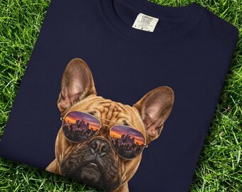 May include: A navy blue t-shirt featuring a graphic print of a tan French Bulldog wearing aviator sunglasses. The lenses of the sunglasses reflect a city skyline at sunset. The shirt has a white neck label with the text Comfort Colors.