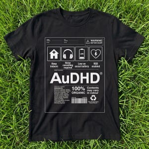 Könnte beinhalten: Ein schwarzes Kurzarm-T-Shirt mit einem weißen Grafikdruck, der einem Versandetikett ähnelt. Das Design enthält Symbole für ein Haus, Kopfhörer, eine Batterie und ein Herz sowie den Text AuDHD, 100% ORGANIC und verschiedene Zutatenlisten.