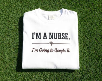 May include: A white t-shirt featuring black text that reads I'M A NURSE. followed by a horizontal line with a heartbeat pulse graphic in the centre and the text I'm Going to Google It. printed in a smaller, cursive-style font below the line.