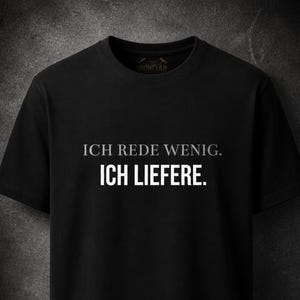 Könnte beinhalten: Schwarzes T-Shirt mit dem deutschen Text "ICH REDE WENIG. ICH LIEFERE." in Weiß. Das Shirt hat einen Rundhalsausschnitt und kurze Ärmel. Der Hintergrund ist ein dunkles, strukturiertes Grau.
